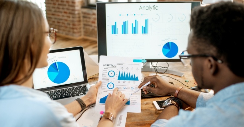 Two professionals examining graphs on a computer screen, discussing hotel marketing KPIs and their impact on strategy.