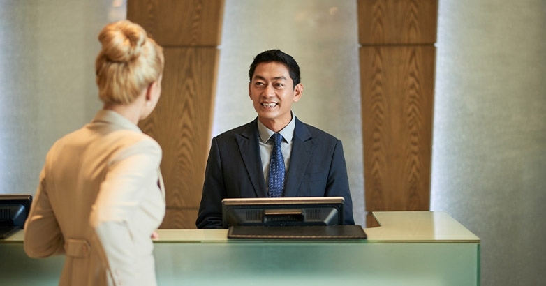 A man and woman stand at a hotel reception desk, showcasing marketing KPIs related to occupancy rates.